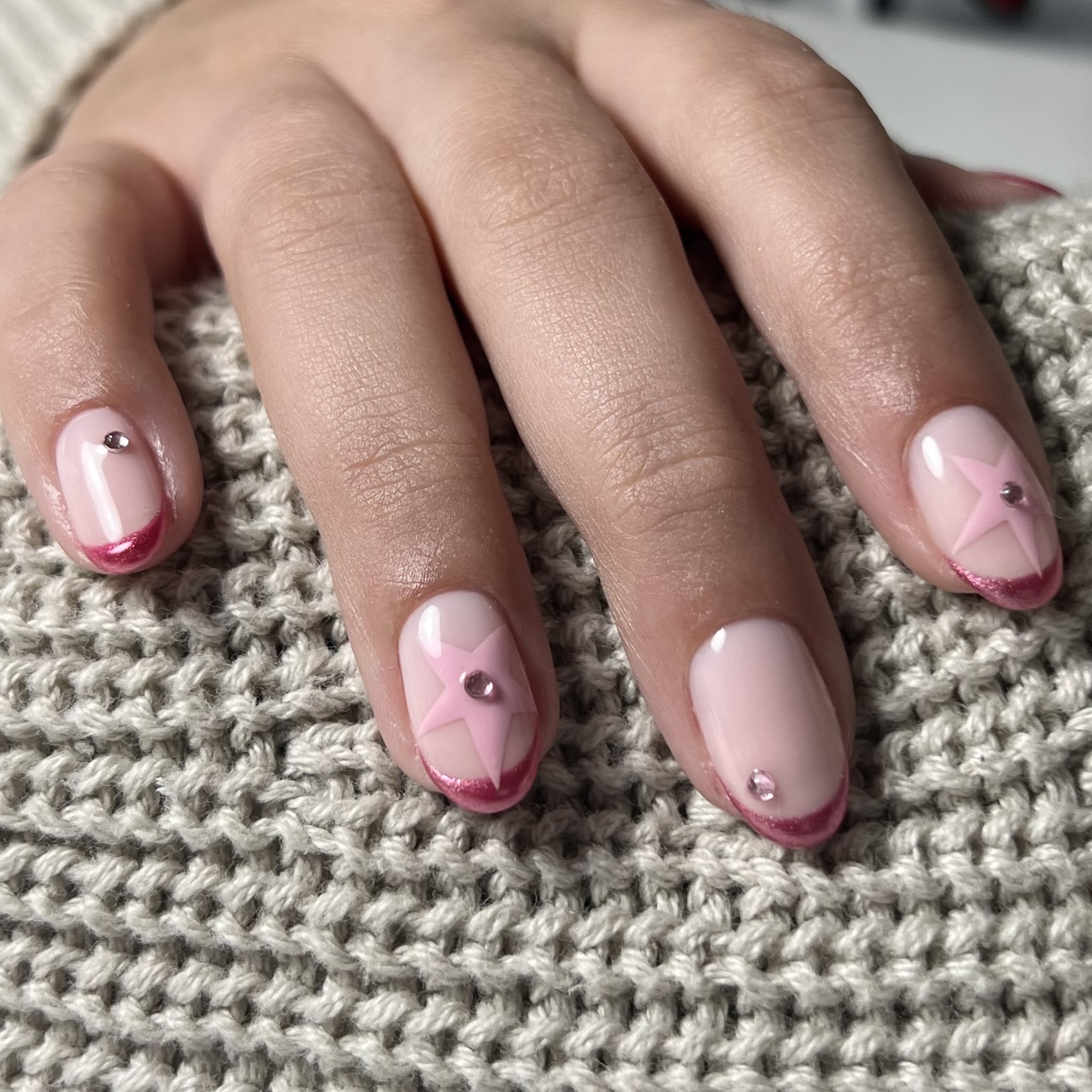 Roze French tips met een sterretje en een steentje, op een grijze gebreide mouw