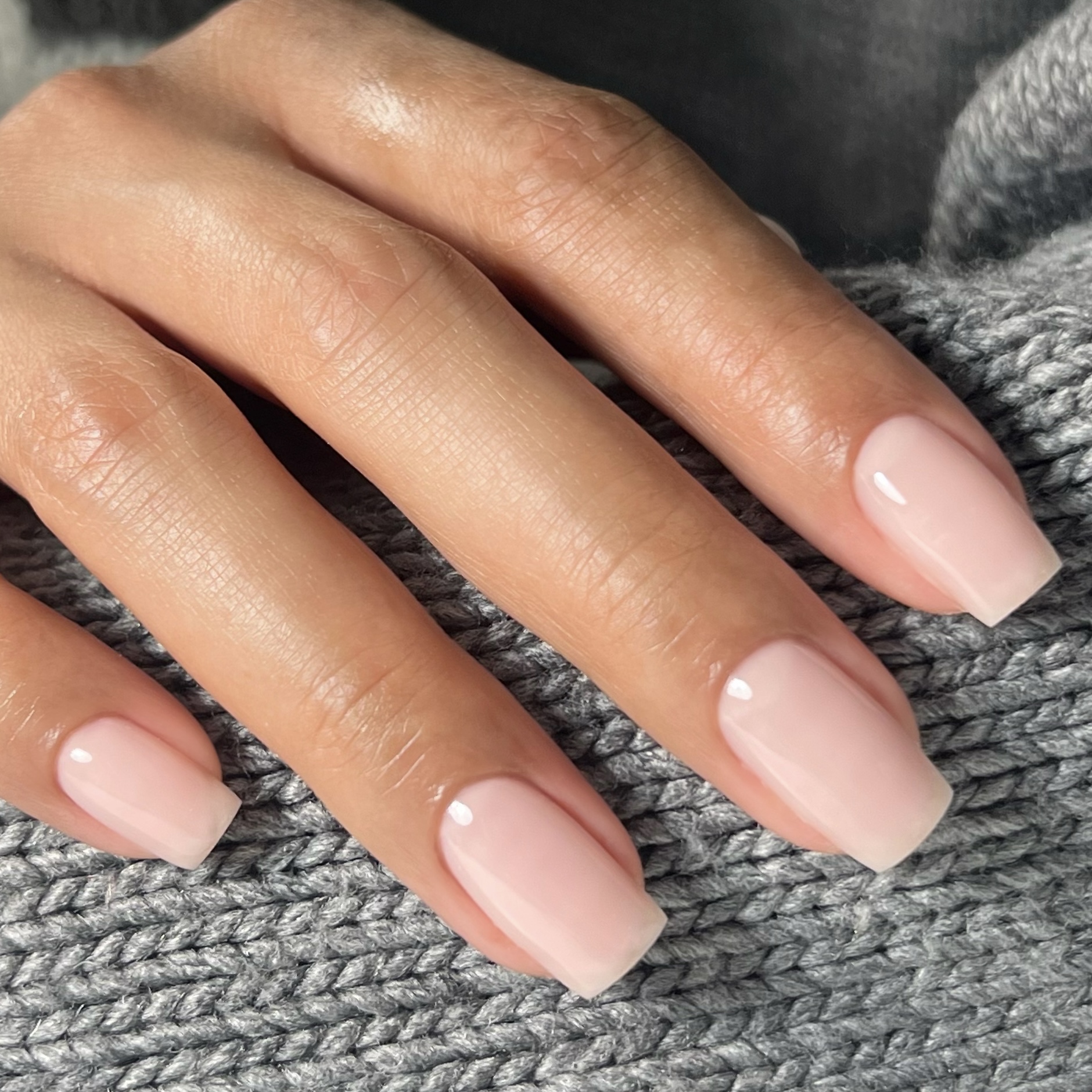 Melkachtig nude gelnagels, vierkant gevijld, op een grijze gebreide mouw